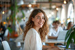 © Kowit - Successful Female Entrepreneur Smiling While Working on Laptop in Bright Startup Office with Team in Background
