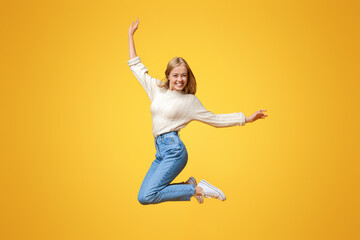 Enjoying youth. Cute teenage girl having fun jumping in air on orange background