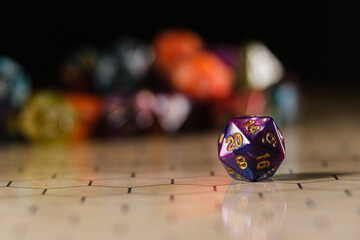 a blue and purple marbled twenty-sided D20 dice with gold numbers, showing the number 20, sitting on a hexagonal tabletop gaming board with a variety of different types of dice in the background. 