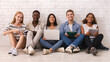 © Prostock-studio - Cheerful group of international students studying over white brick wall, using laptop, books, digital tablets, panorama