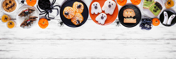 Wall Mural - Spooky Halloween breakfast top border over a white wood banner background with copy space. Above view. Assortment of pancakes, toast, oatmeal and fruit.