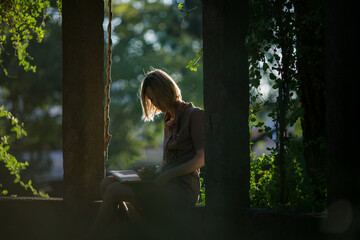 A woman writes notes in a notebook while sitting in a sunlit gazebo.