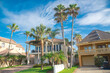 © trongnguyen - Row of two-story beach house vacation home rental property with porch, clay tile roofs with line of palm trees under sunny cloud blue sky near downtown South Padres Island, travel destinations
