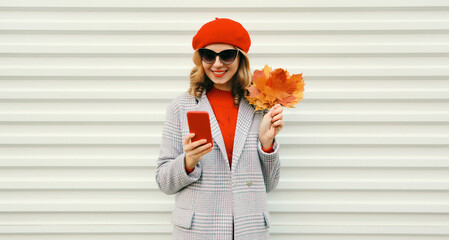 Wall Mural - Autumn portrait stylish happy smiling young woman with phone, beautiful girl holding yellow leaves