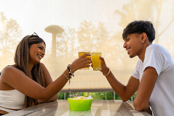 young couple toasting an aperitif sitting at a table in a rustic outdoor bar