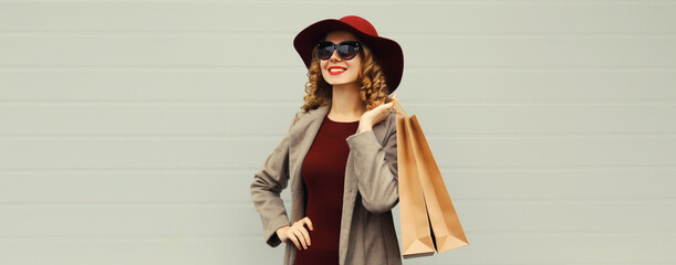 Wall Mural - Autumn portrait of beautiful young woman with shopping bag, stylish girl in coat on gray background