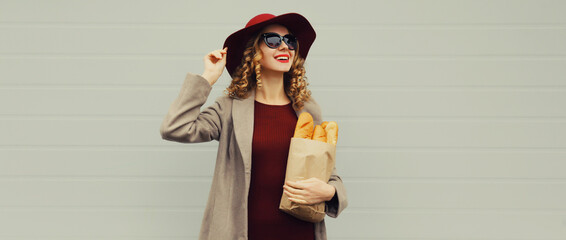 Wall Mural - Beautiful happy smiling young woman holding grocery shopping paper bag with white bread baguette