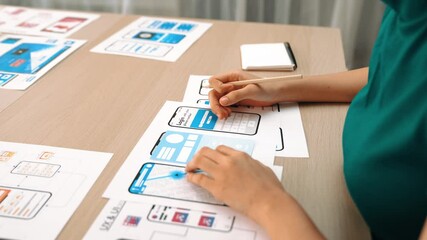 Startup company employee planning for user interface prototype for mobile application or website in office with model of program on desk. UX UI designer consider user friendly interface plan. Synergic