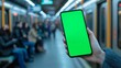 © Lumos Maxima - Woman is holding a smartphone with green or chroma key screen in blurred subway train station blurred background, perfect for showcasing apps and mobile technology, travel and navigation concept