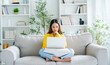 © Monster Ztudio - Young Asian woman using laptop while seated on couch at home