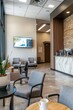© Starlight - A spacious clinic waiting room with multiple seating areas, a wall-mounted TV showing a health program, and a coffee station, Generative AI