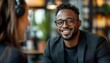 © Nattapat - Cheerful African American man with glasses and a black suit engaging with an unrecognizable female guest at a podcast table in a studio, medium shot