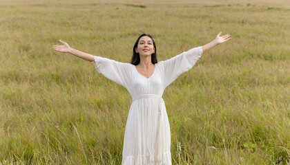 Woman in a dress standing with arms outstretched in the middle of an open field 