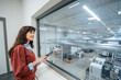 © Westend61 - Smiling businesswoman holding tablet PC and looking out of glass window in factory
