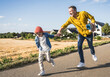© Westend61 - Cheerful man and boy holding hands and running on road