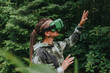 © Westend61 - Woman gesturing and watching through futuristic glasses at forest