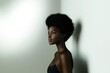 © tino - A woman with a beautiful and voluminous afro hairstyle is standing confidently in front of a stark white wall, creating a striking contrast