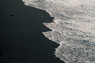 Black sand beach and white waves at sunrise in Bali, Indonesia