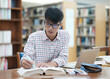© ijeab - Young Asian male sitting inside a library alone doing research. Man working on a project. Young man doing research for a case.
