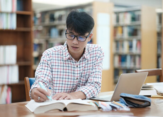 young asian male sitting inside a library alone doing research. man working on a project. young man 