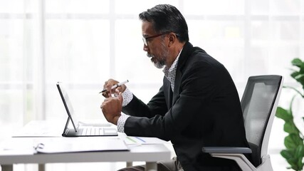 Wall Mural - Experienced executive using tablet in contemporary office setting. Senior businessman presenting online, discussing and making hand gestures, and using a laptop during a virtual meeting in office.