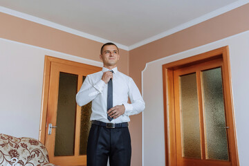 Wall Mural - A man in a suit is standing in front of a door, getting ready to tie his tie