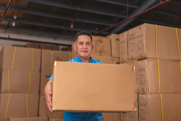 Middle aged warehouse clerk carrying a large cardboard box in a storage area