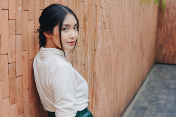 Beautiful young Asian woman in a green sequined skirt stands in front of a brick wall.