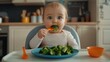 © Vladislav - A cute little girl sits in her high chair and eats broccoli. She holds an orange spoon with steamed green vegetables on it and her big blue eyes look at the camera. Healthy eating for kids