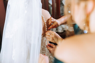 A bride is getting ready for her wedding and her bridesmaids are helping her. The bride is wearing a white veil and a white dress