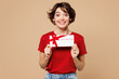© ViDi Studio - Young shocked surprised happy woman she wear red t-shirt casual clothes hold gift certificate coupon voucher card for store isolated on plain pastel light beige background studio. Lifestyle concept.