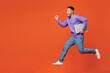 © ViDi Studio - Full body young IT man of African American ethnicity wear purple sweatshirt casual clothes jump high hold closed laptop pc computer run fast isolated on plain red orange background. Lifestyle concept.