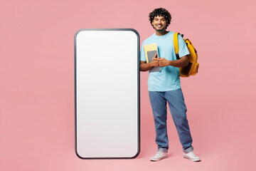 Wall Mural - Full body young Indian boy student wear blue casual clothes backpack bag hold books big huge blank screen mobile cell phone isolated on plain pink background. High school university college concept.