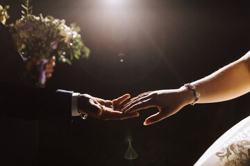 Poster - A couple is holding hands in a dark room. The bride is wearing a white dress. The man is wearing a blue suit