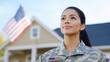© Kateryna - A proud female soldier standing in front of her home, looking up at the sky with a thoughtful expression. She is dressed in full camouflage uniform, with the American flag patch pr