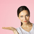 © vgstudio - Portrait image of businesswoman showing something or copy space for some product. Brunette woman holding, giving on hand palm in studio ad concept, over rose pink background.