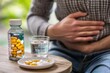 © DK_2020 - Person holding their stomach with a bottle of antacids and a glass of water on a table, medications to relieve stomach pain and discomfort
