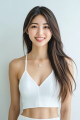 A beautiful Japanese woman with long flowing hair smiles radiantly in a white sleeveless top. The simplicity of the outfit and her joyful expression make.