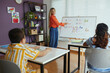 © DragonImages - Teacher engaging children in learning alphabet letters with colorful educational materials displayed on whiteboard at classroom with bright window and organized bookshelves