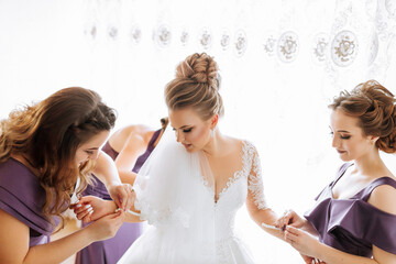 Three women are getting ready for a wedding. One of them is putting on a wedding ring. The other two women are helping her