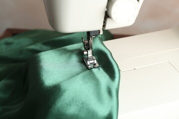 Poster - Sewing machine with green fabric on light background, closeup