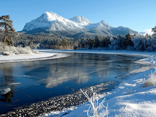 Wall Mural - A frozen river with snow on the mountains in the background. The water is still and calm. The scene is peaceful and serene