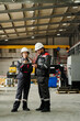 © Clique Images - Workers wearing protective gear in large manufacturing facility discussing project details while standing near industrial equipment