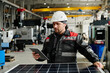 © TrueFrame Collective - Engineer wearing a hard hat and work uniform examining solar panels. Industrial setting