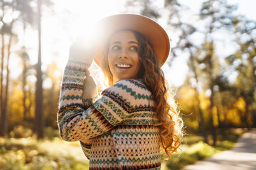 A joyful woman in a patterned sweater and hat enjoying a sunny autumn day in a vibrant forest. Travel, tourism, weekend.