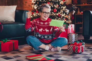 Sticker - Full size body photo of funny retired woman in deers print jumper sitting on carpet and reading mail at christmas atmosphere indoors