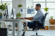 © Hanna - Man using computer at modern office desk with prosthetic leg in bright workspace during daytime