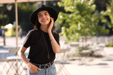 Canvas Print - Beautiful young woman in stylish black hat on city street, space for text