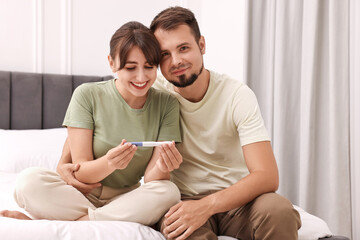 Poster - Happy young couple with pregnancy test on bed at home