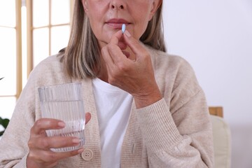 Canvas Print - Senior woman with glass of water taking pill at home, closeup